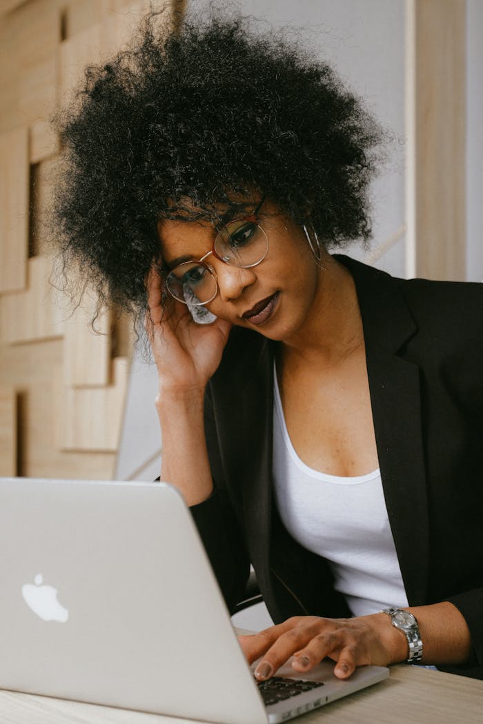 The Art of Drawing Readers In: Your attractive post title goes here Businesswoman with afro hairstyle working on a laptop, looking focused and professional in an office setting.